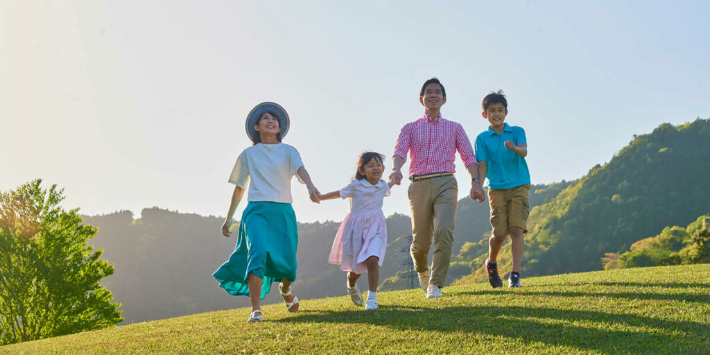 a family of four walking in the grass under a blue sky with a picturesque view in the background