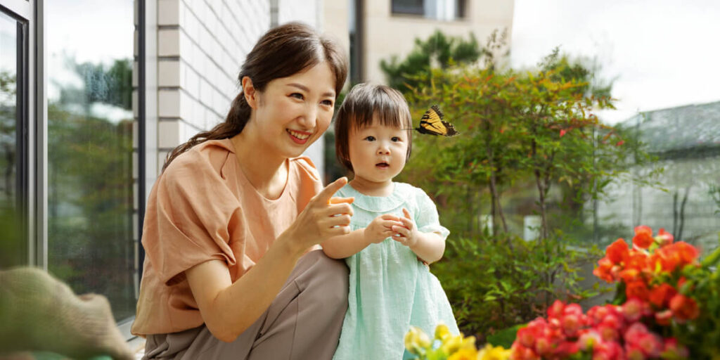 a mother with her daughter looking at a butterfly hovering above flowers