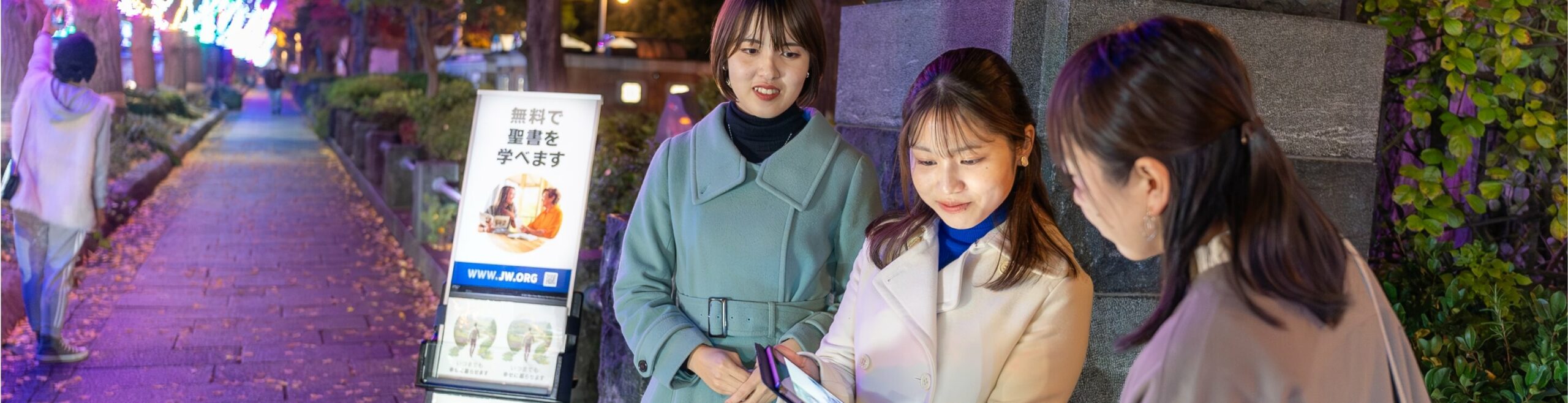 home-footer two women standing in front of a public witnessing cart showing a woman something on an electronic device